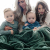 A mother and her two sons and daughter sit under a Luxury Extra Large Oversized Throw Hunter Green Colored Lush Saranoni Blanket. The soft blanket is an extra large throw blanket and has a soft faux fur feeling.