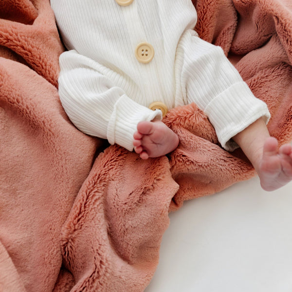 A newborn lays on top of a Clay Colored Lush Saranoni Blanket. The soft blanket is a small blanket and a baby blanket.