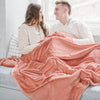 A husband and wife sit while holding a Luxury Extra Large Oversized Throw Clay Colored Lush Saranoni Blanket. The soft blanket is an extra large throw blanket and has a soft faux fur feeling.