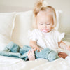 A little girl sits up with a Dew (light blue) Colored Lush Saranoni Blanket on her lap. The soft blanket is a small blanket and a baby blanket or toddler blanket.