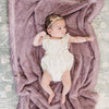 A baby girl lays on a Luxury Receiving Bloom (dusty purple) Colored Lush Saranoni Blanket. The soft blanket is a small blanket and a baby blanket or toddler blanket.