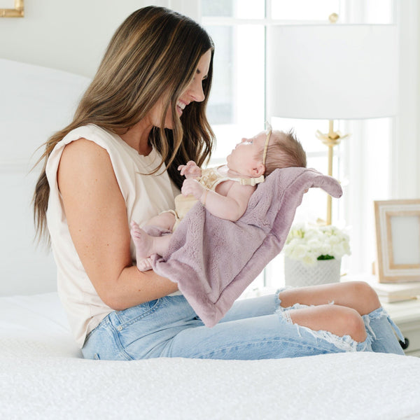 A mother holds her baby girl in Bloom (dusty purple) Colored Lush Saranoni Blanket. The soft blanket is a small blanket and a baby blanket or toddler blanket.