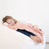 A little girl lays under a Luxury Receiving Blossom (light peachy pink) Colored Lush Saranoni Blanket. The soft blanket is a small blanket and a baby blanket or toddler blanket.