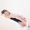 A little girl lays under a Blossom (light peachy pink) Colored Lush Saranoni Blanket. The soft blanket is a small blanket and a baby blanket or toddler blanket.