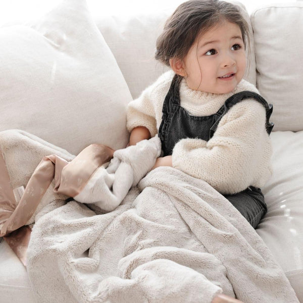 Dainty Floral@A little girl sitting on a couch holds her silky toddler blanket.