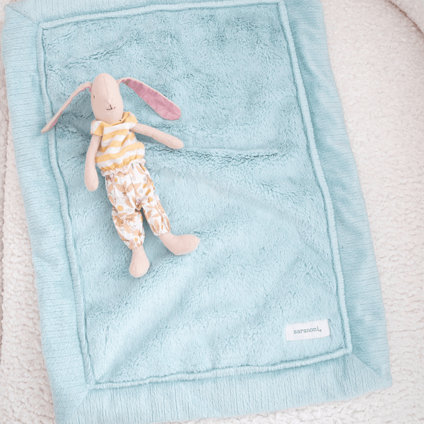 A stuffed animal bunny lays on a Dew (light blue) Colored Lush Saranoni Blanket. The soft blanket is a small blanket and a baby blanket.