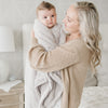 A mother holds her baby boy in a Receiving Feather (light gray) Colored Lush Saranoni Blanket. The soft blanket is a small blanket and a baby blanket or toddler blanket.