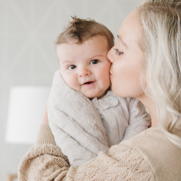 A mother holds her baby boy in a Receiving Feather (light gray) Colored Lush Saranoni Blanket. The soft blanket is a small blanket and a baby blanket or toddler blanket.