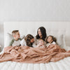 A mother and her two sons and two daughters sit under a Luxury Extra Large Oversized Throw Rosy (dusty peach) Colored Lush Saranoni Blanket. The soft blanket is an extra large throw blanket and has a soft faux fur feeling.