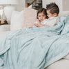 A brother and sister sit while holding a Luxury Extra Large Oversized Throw Dew (light blue) Colored Lush Saranoni Blanket. The soft blanket is an extra large throw blanket and has a soft faux fur feeling.