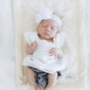 A little baby girl lays on top of a Natural (off-white) Colored Lush Saranoni Blanket. The soft blanket is a small blanket and a baby blanket.