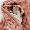 A baby girl lays in a Luxury Receiving Clay Colored Lush Saranoni Blanket. The soft blanket is a small blanket and a baby blanket or toddler blanket.