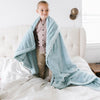 A little boy is wrapped in a Luxury Toddler Dew (light blue) Colored Lush Saranoni Blanket. The soft blanket is a toddler blanket or baby blanket.