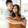 A couple holds a Luxury Extra Large Oversized Throw Camel (light yellowish brown) Colored Lush Saranoni Blanket. The soft blanket is an extra large throw blanket and has a soft faux fur feeling.