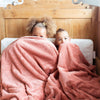 A sister and brother sit while holding a Luxury Extra Large Oversized Throw Clay Colored Lush Saranoni Blanket. The soft blanket is an extra large throw blanket and has a soft faux fur feeling.