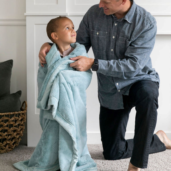 A father wraps his son in a Luxury Toddler Dew (light blue) Colored Lush Saranoni Blanket. The soft blanket is a toddler blanket or baby blanket.