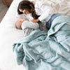 A mother and son lay under a Luxury Extra Large Oversized Throw Dew (light blue) Colored Lush Saranoni Blanket. The soft blanket is an extra large throw blanket and has a soft faux fur feeling.