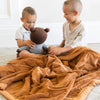 Two little boys who are brothers sit under a Luxury Toddler Camel (light yellowish brown) Colored Lush Saranoni Blanket. The soft blanket is a toddler blanket or baby blanket.