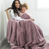 A mother holds her daughter while holding a Luxury Extra Large Oversized Throw Bloom (dusty purple) Colored Lush Saranoni Blanket. The soft blanket is an extra large throw blanket and has a soft faux fur feeling.