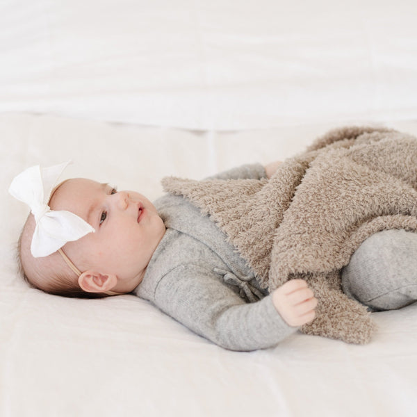 Baby girl with white bow playing with neutral, beautiful BAMBONI MINI BLANKETS - Saranoni