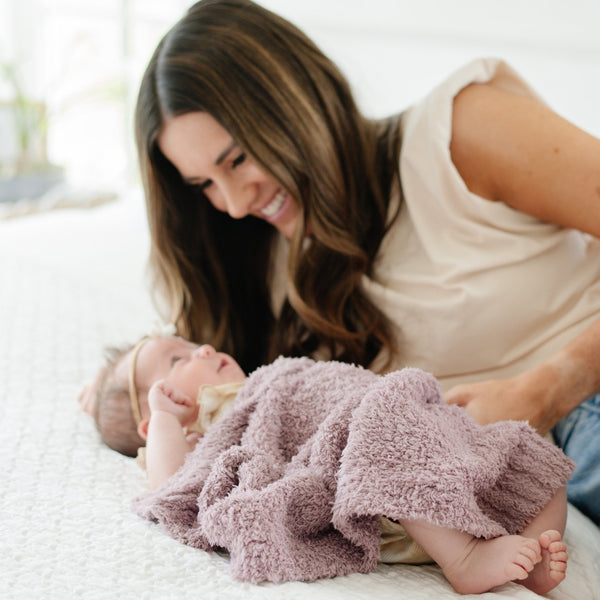 Mom and newborn baby girl snuggling on bed in adorable purple BAMBONI MINI BLANKETS - Saranoni