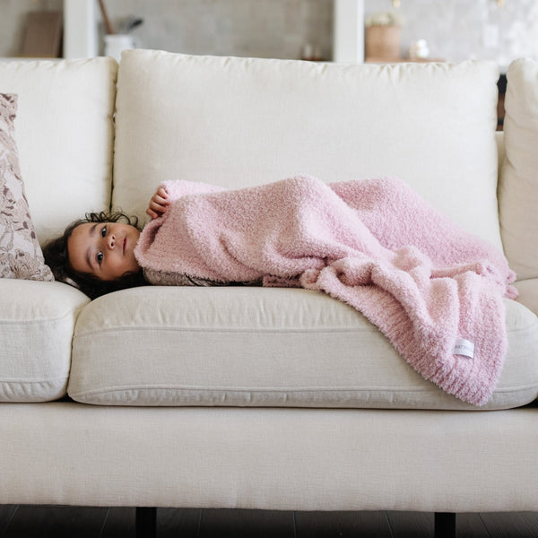 Little girl laying on a beautiful couch with light pink BAMBONI® RECEIVING BLANKETS - Saranoni