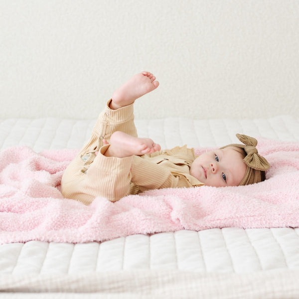 Little girl laying on super soft and stretchy, light pink BAMBONI RECEIVING BLANKETS - Saranoni