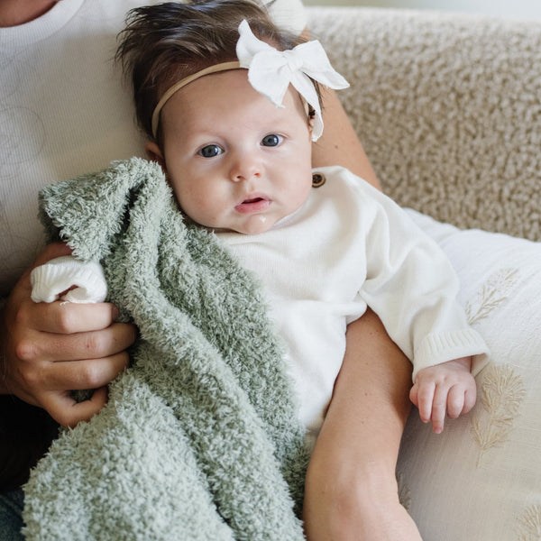 Baby girl holding on to super soft and stretchy Sage BAMBONI® RECEIVING BLANKETS - Saranoni