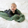 Adorable baby boy smiling on bed, snuggling on Olive BAMBONI RECEIVING BLANKETS - Saranoni