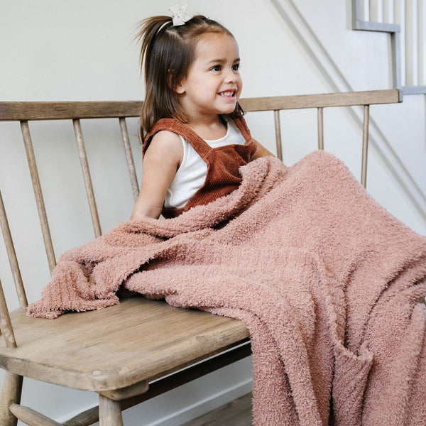 Young girl sitting on bench wrapped in stretchy soft French Rose BAMBONI TODDLER BLANKETS - Saranoni