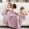 Three siblings sit with a Bamboni® blanket by Saranoni. This ultra-soft blanket is a light purple blanket and made from a premium blend of bamboo rayon and poly microfiber, offering a lightweight, breathable, and fluffy feel. Perfect as a toddler blanket, luxury blanket, or soft blanket, it adds warmth and elegance to any bedroom and is a kids blanket. Designed for ultimate comfort, this buttery-soft Saranoni blanket is ideal for gifting. Enjoy this cozy blanket for years to come!