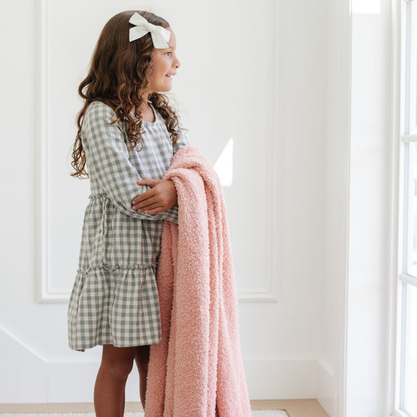 Little girl smiling, looking out the window with her favorite Peach BAMBONI® TODDLER BLANKETS - Saranoni