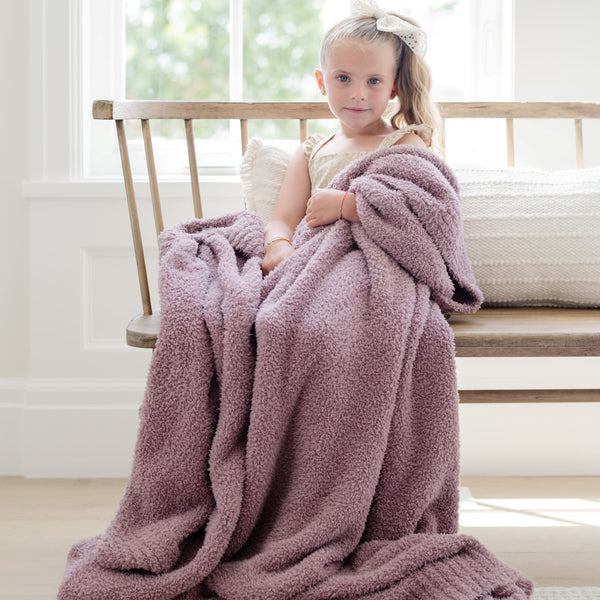 A little girl holds a Bamboni® blanket by Saranoni. This ultra-soft blanket is a light purple blanket and made from a premium blend of bamboo rayon and poly microfiber, offering a lightweight, breathable, and fluffy feel. Perfect as a toddler blanket, luxury blanket, or soft blanket, it adds warmth and elegance to any bedroom and is a kids blanket. Designed for ultimate comfort, this buttery-soft Saranoni blanket is ideal for gifting. Enjoy this cozy blanket for years to come!