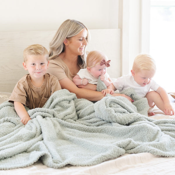 Mom and three adorable kids snuggling together on bed with extra soft Sage BAMBONI® XL BLANKETS - Saranoni