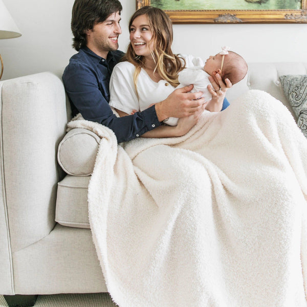 New family snuggled together on couch in IvoryBAMBONI XL BLANKETS - Saranoni