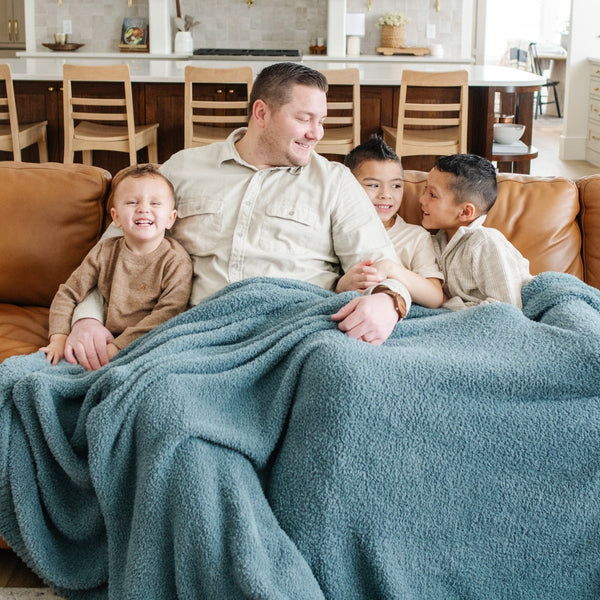 Dad and three adorable boys snuggling on couch with Spruce BAMBONI XL BLANKETS - Saranoni