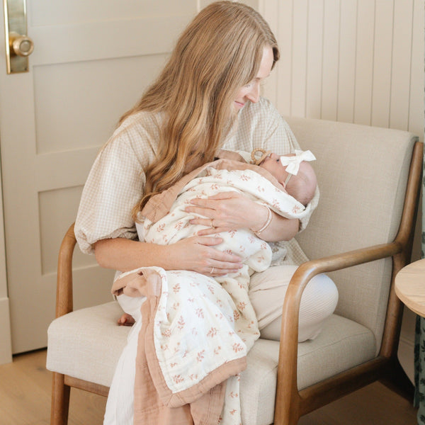 Mother holding her baby daughter wrapped in a soft and breathable bamboo rayon muslin quilt with a stunning pattern, perfect for year-round comfort and style.