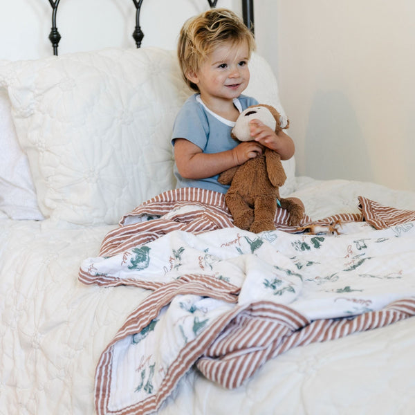 Little boy laying in bed with a cozy and lightweight, adorable printed bamboo muslin quilt. 