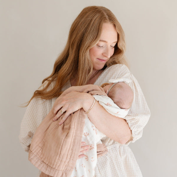 Mother holding her baby girl wrapped in a beautiful and soft bamboo muslin quilt. 