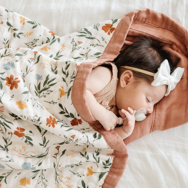 Baby girl wrapped cozily in a comfortable, multi-colored floral bamboo muslin quilt. 