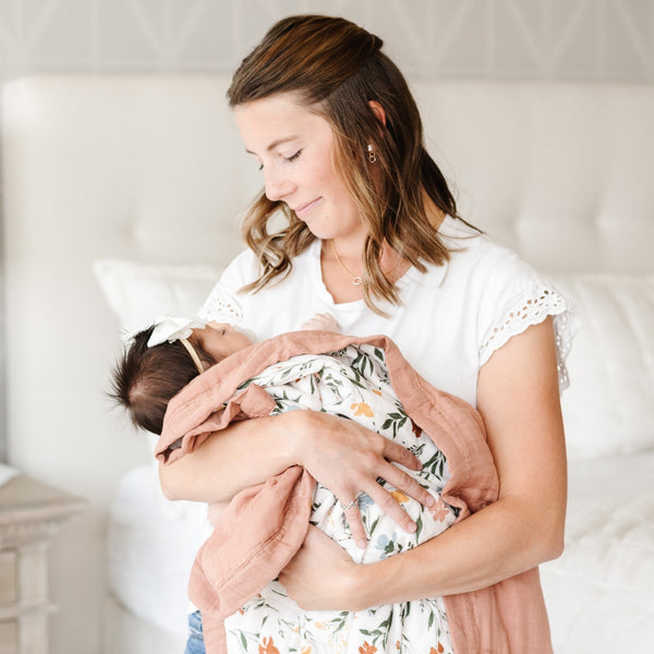 Mother holding daughter wrapped in a soft and cozy floral bamboo muslin quilt. 