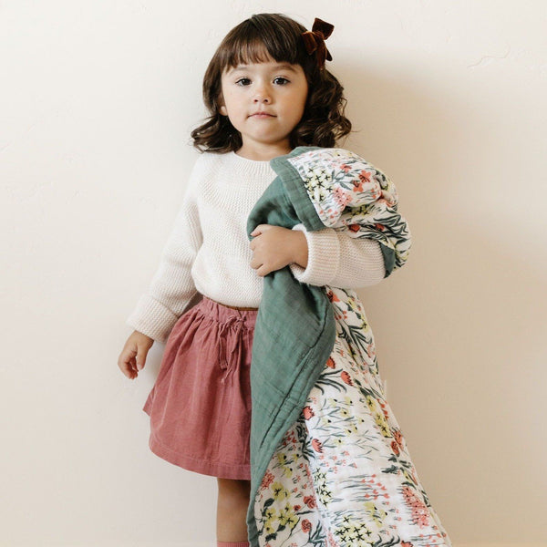 Little girl holding an adorable, floral printed bamboo muslin quilt. 