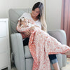 Mother and daughter snuggling together with a coral and white floral print muslin quilt. 