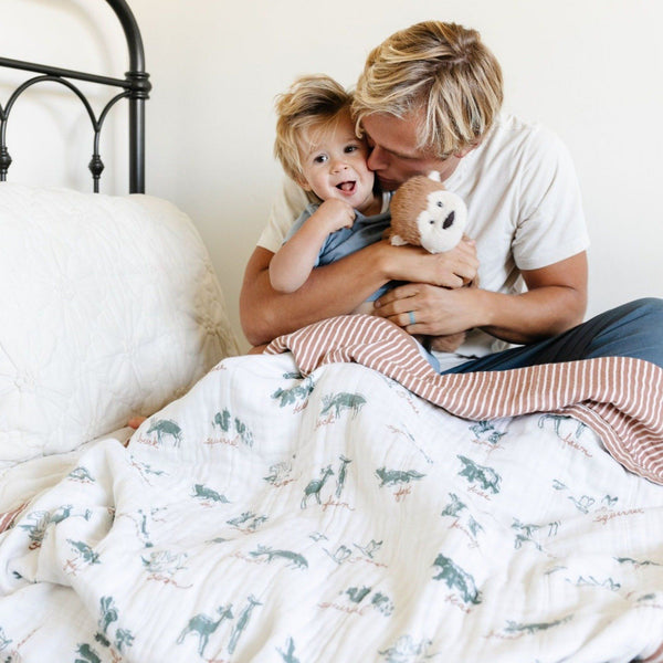 Father and son snuggling in bed with a light and airy bamboo rayon muslin quilt for kids, featuring a cute pattern that combines comfort and fun