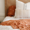 Elegant details of an orange, swiss cross bamboo muslin quilt and pillowcase.