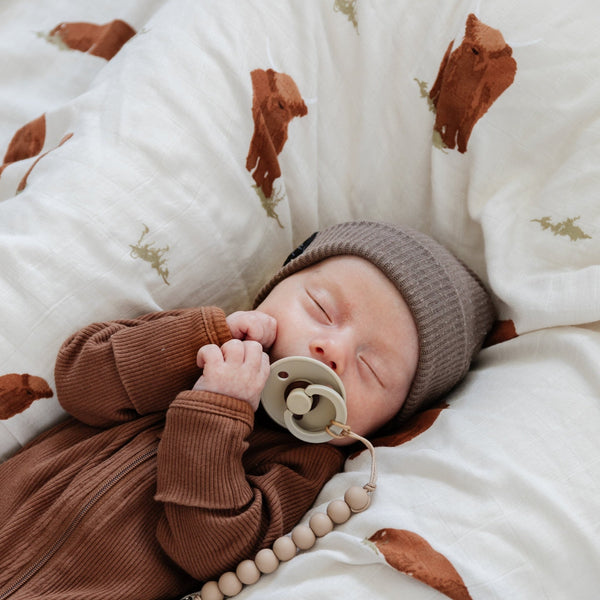 Baby boy snuggling amidst a soft and breathable bamboo muslin swaddle, perfect for wrapping your baby in gentle comfort.