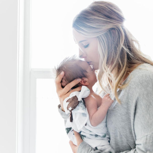 Mother nestling her newborn baby wrapped in a soft and cozy baby swaddle. 