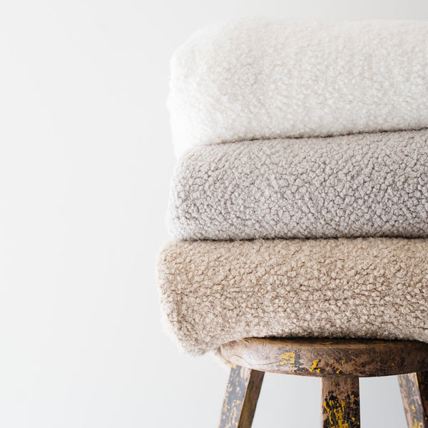 Stack of high-quality boucle blankets in an ivory, cream and tan colors. - Saranoni