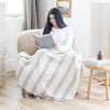 Woman with long dark hair sitting in beige armchair, reading book under white striped xl throw blanket- Saranoni