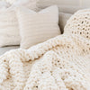 A soft, white Saranoni chunky knit throw blanket. The large knit Saranoni blanket, is made from 100% poly microfiber and drapes beautifully. This luxury throw blanket is both trendy and durable, making it the perfect addition to any space. Ideal for home decor enthusiasts and those seeking a cuddly, soft blanket, this chunky knit blanket combines style and comfort. Keywords: chunky knit throw, soft blanket, knit blanket, large knit blanket, luxury throw blanket.